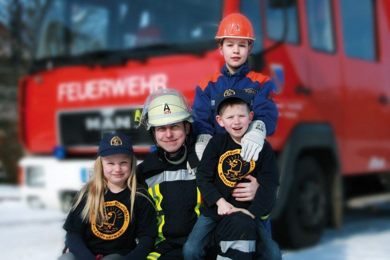 Kinderfeuerwehr und Jugendfeuerwehr mit Feuerwehrmann vor dem Löschfahrzeug